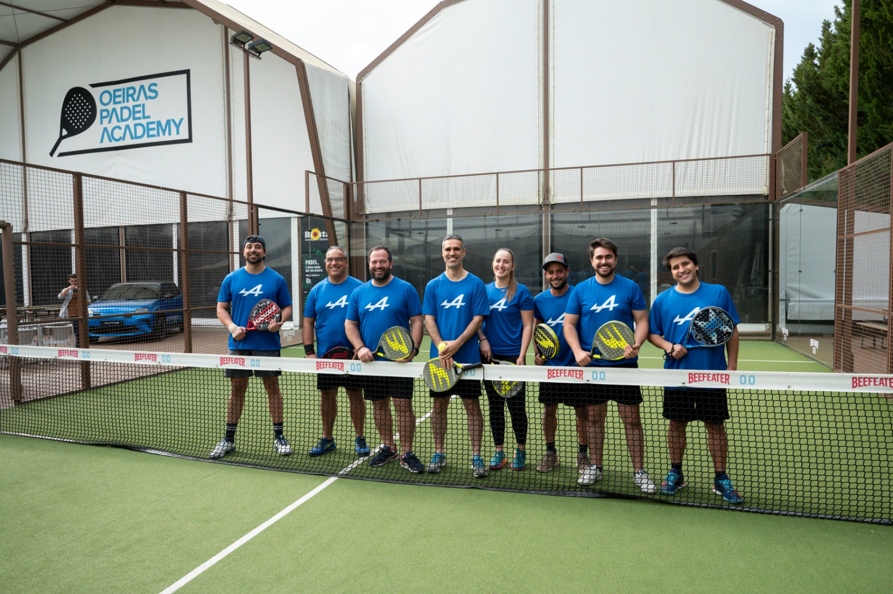 Equipa Alpine alinhada com t-shirts azuis e raquetes no Oeiras Padel Academy