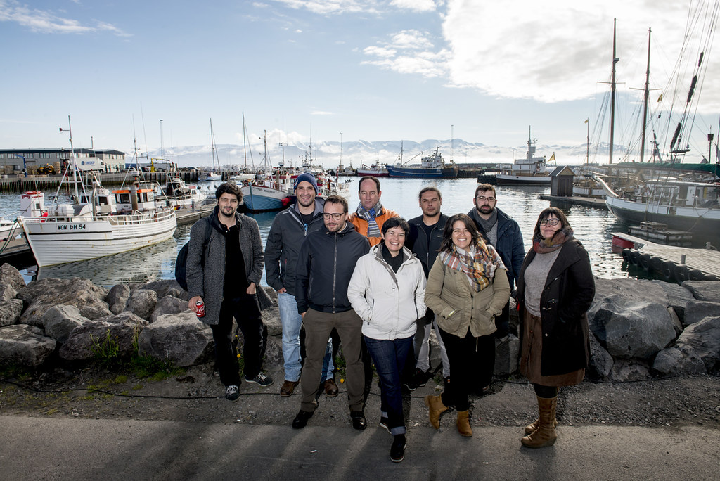 Grupo de jornalistas portugueses fotografados no porto da Islândia com barcos e montanhas ao fundo
