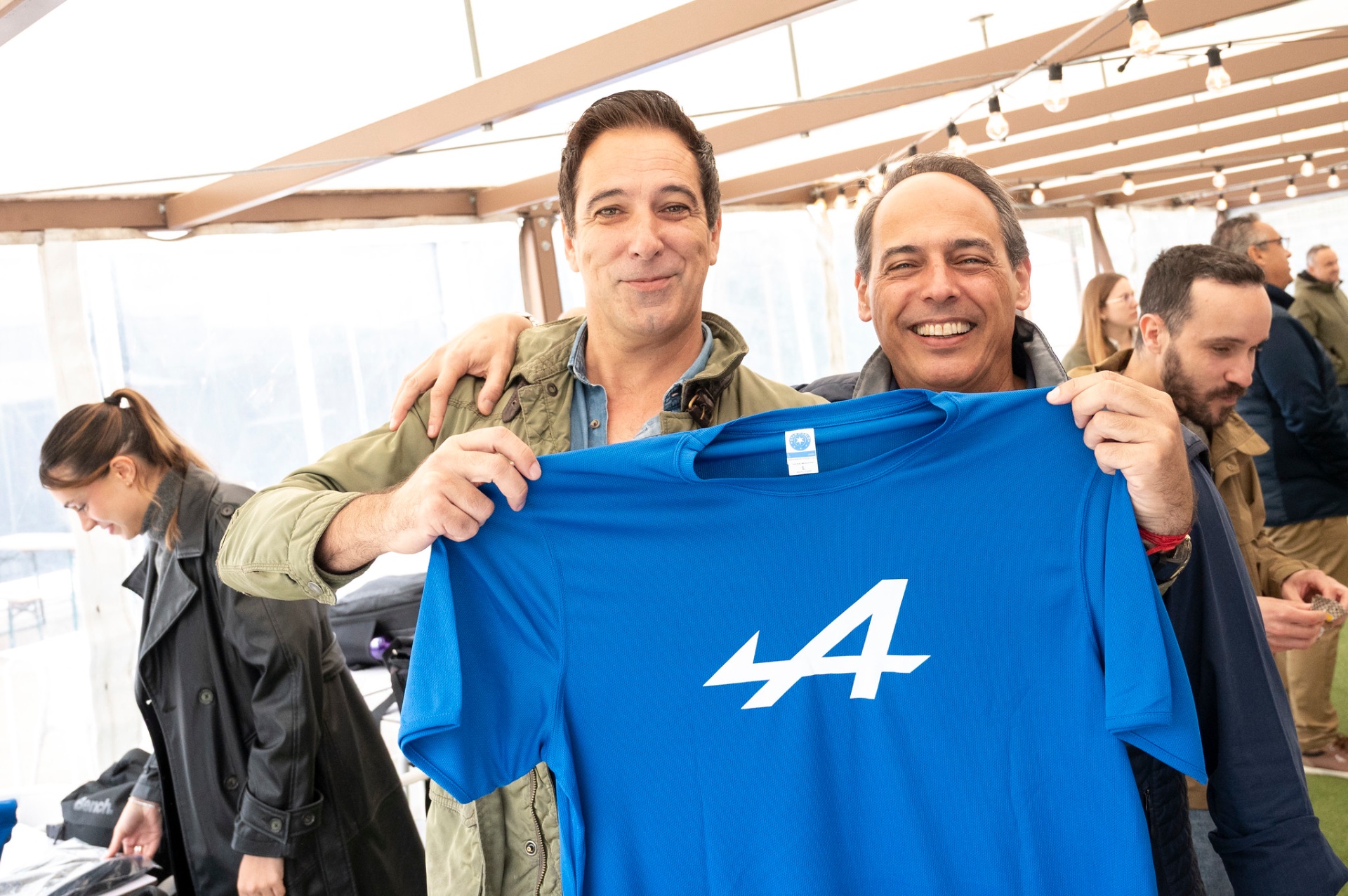 Dois jornalistas sorridentes mostram t-shirt Alpine azul oferecida na ação