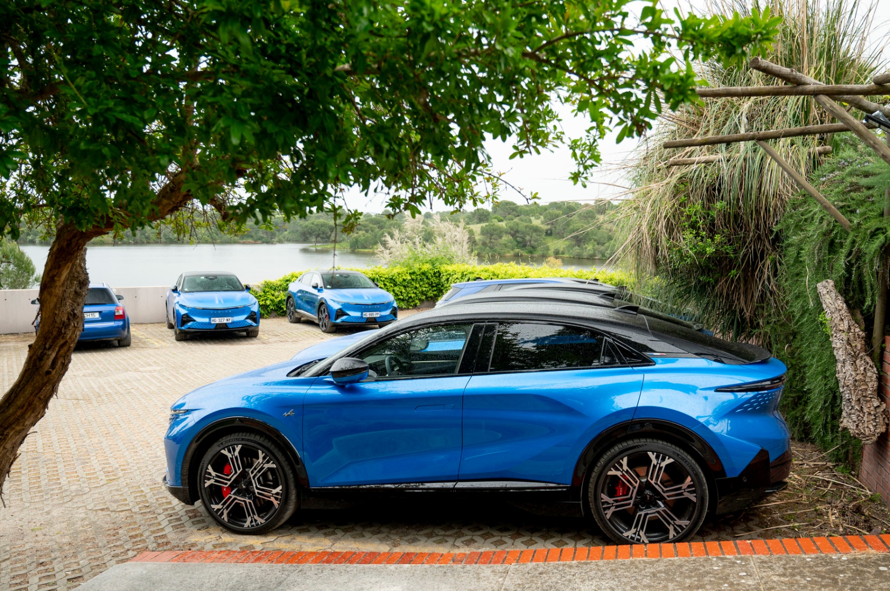 Alpine A390 GT azul em primeiro plano com frota de outros A390 GT estacionados junto à albufeira do Vale do Gaio