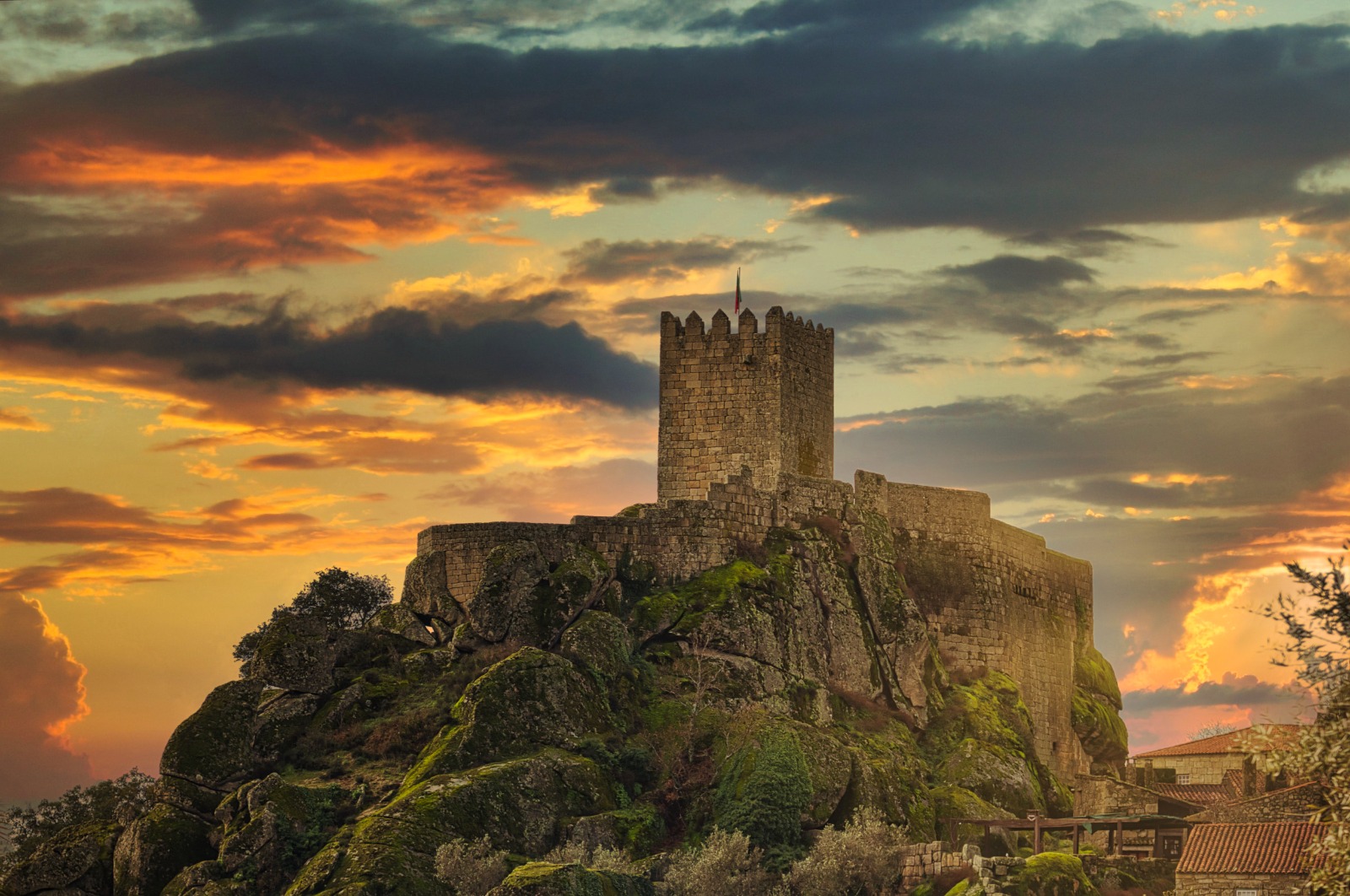 Castelo de Sortelha sobre afloramento rochoso ao pôr do sol, com céu de nuvens alaranjadas