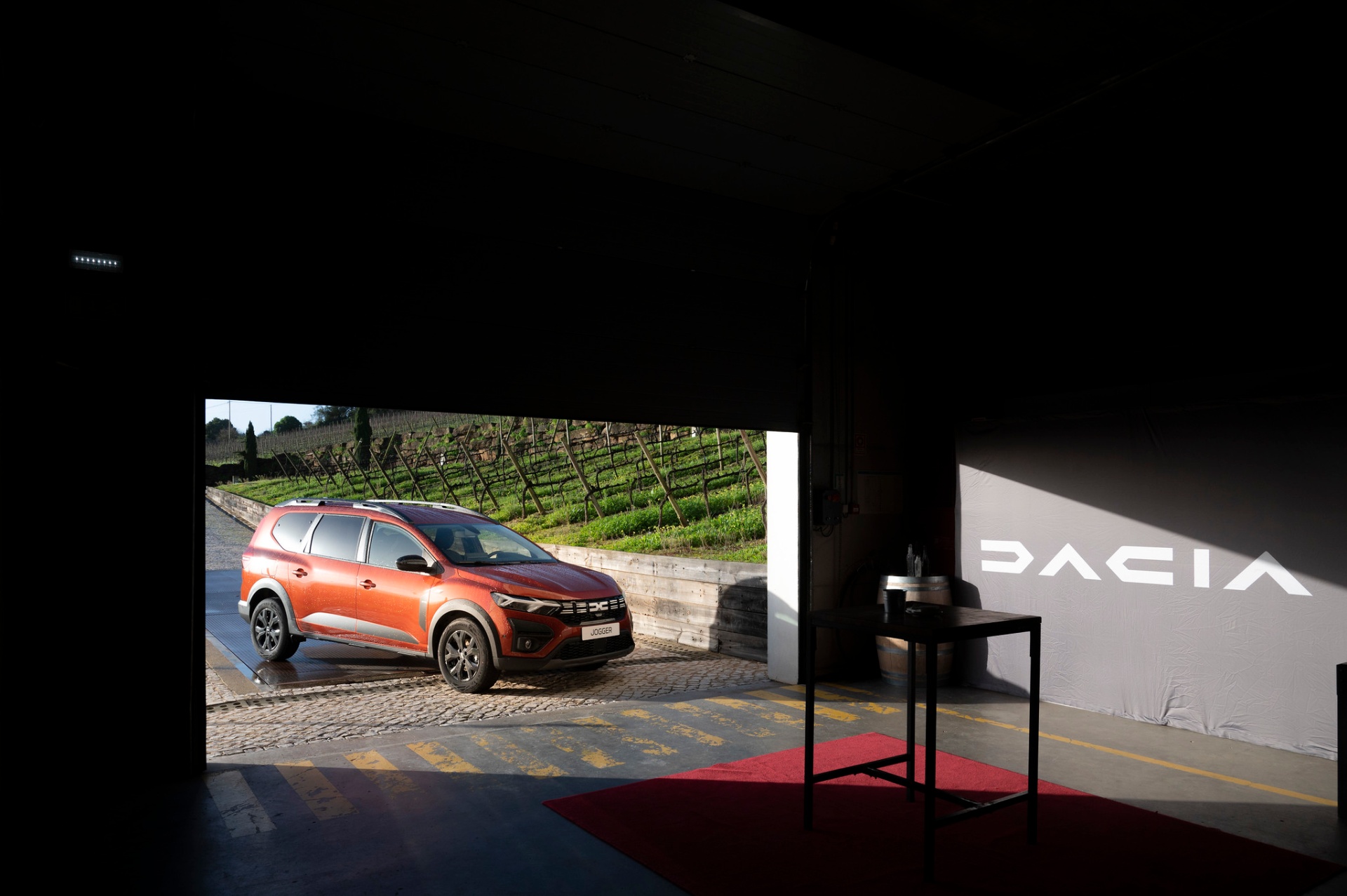 Dacia Jogger laranja enquadrado pelas vinhas da AdegaMãe vistas do interior da adega