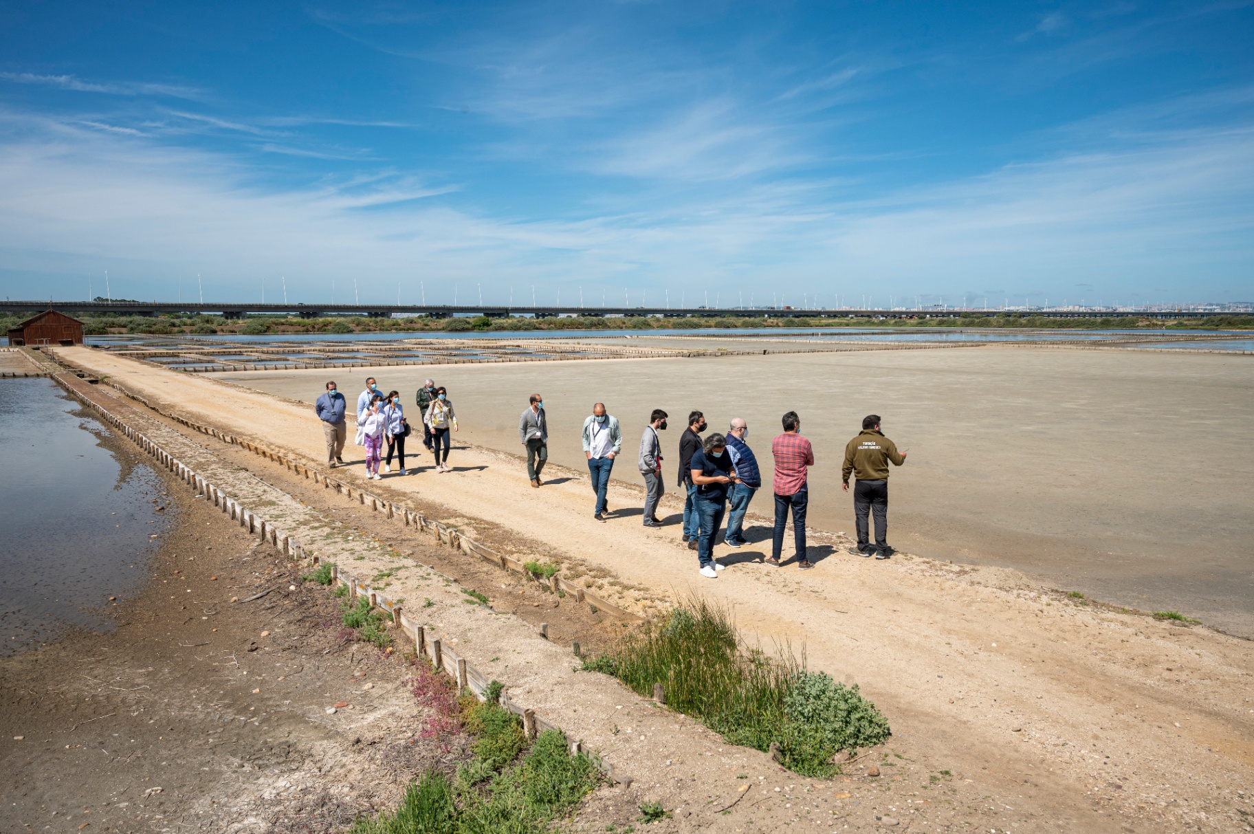 Grupo de jornalistas a percorrer caminho entre salinas em dia de sol