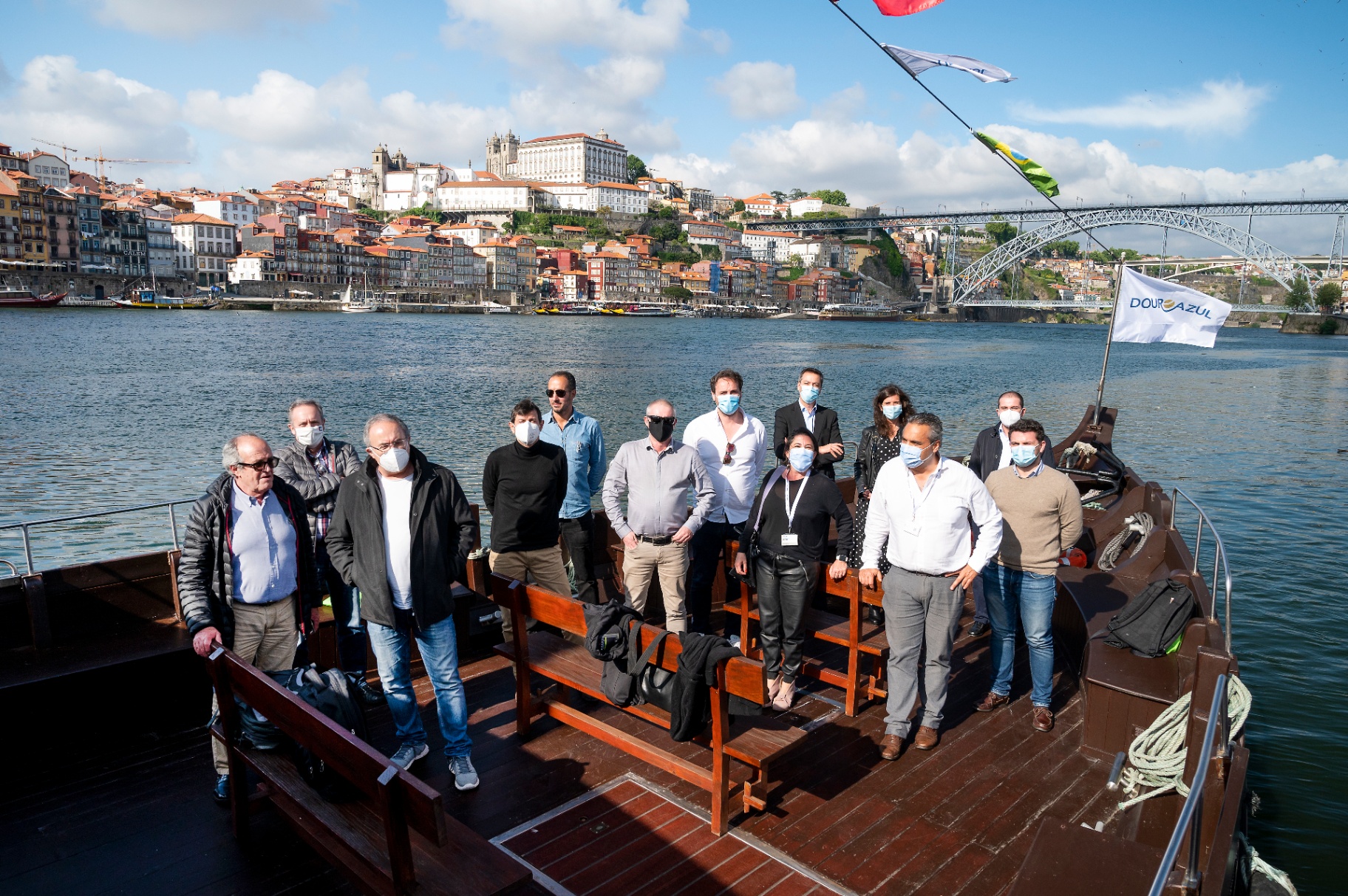 Grupo de jornalistas a bordo de um barco rabelo no Douro, com a Ribeira ao fundo