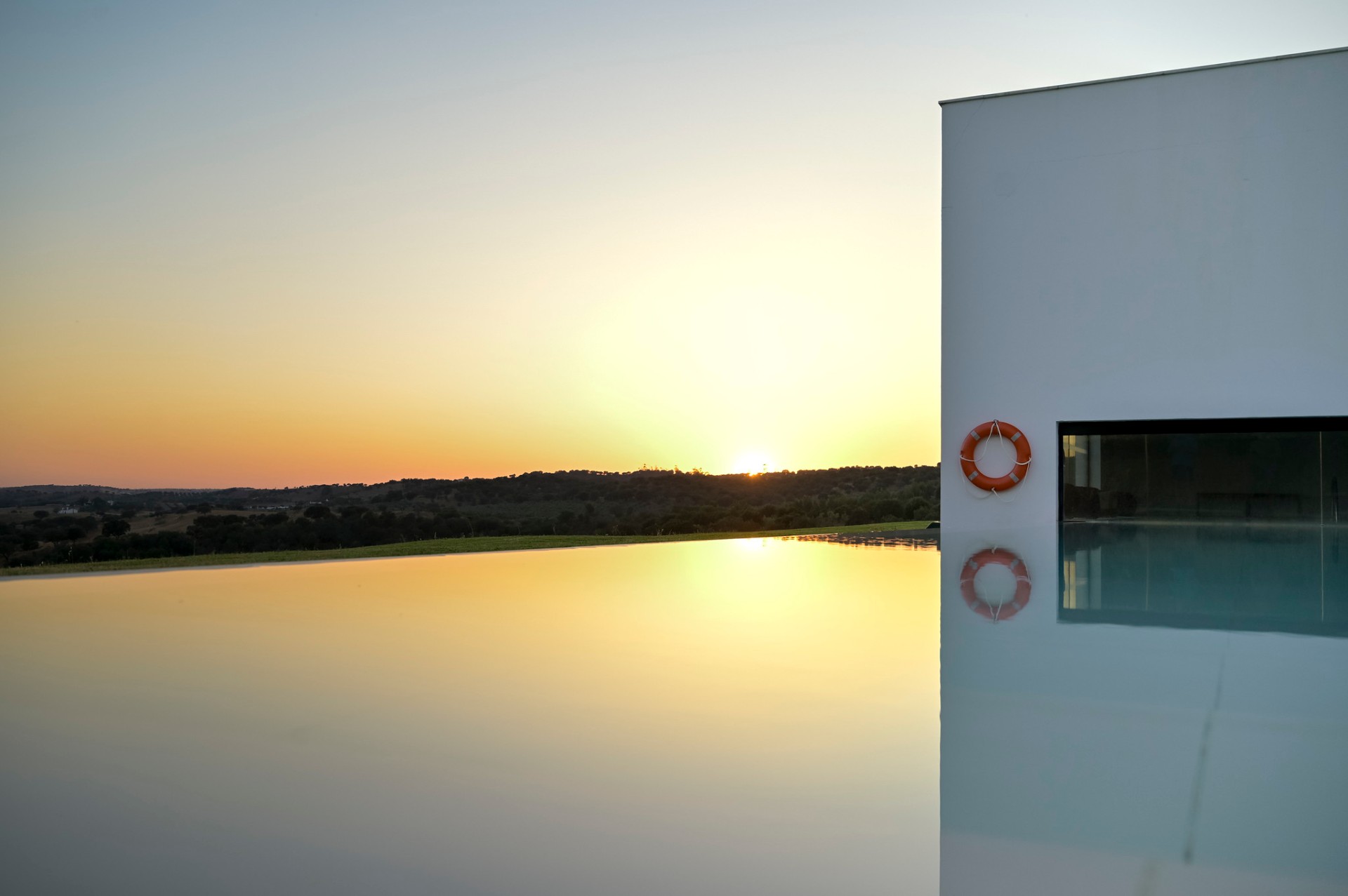 Piscina infinita refletindo o pôr do sol sobre a planície alentejana