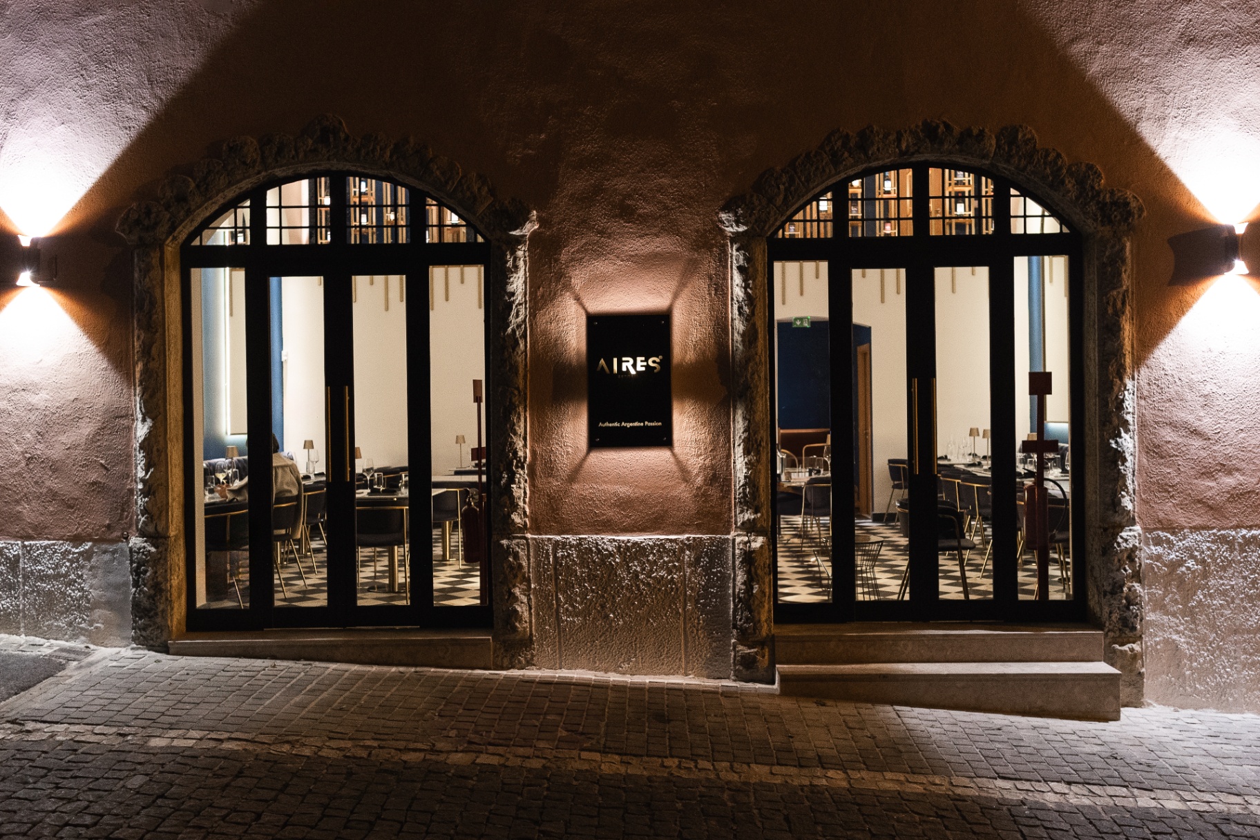Fachada nocturna do Aires Restaurant no Monte Estoril com arcos iluminados e sala visível pelas vidraças