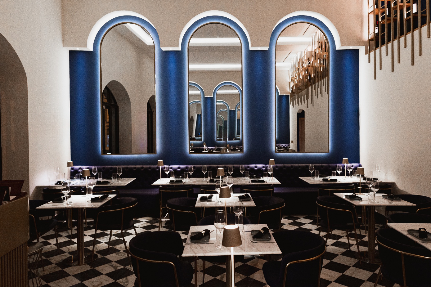 Sala interior do Aires com parede azul, arcos espelhados, banco capitoné e chão xadrez