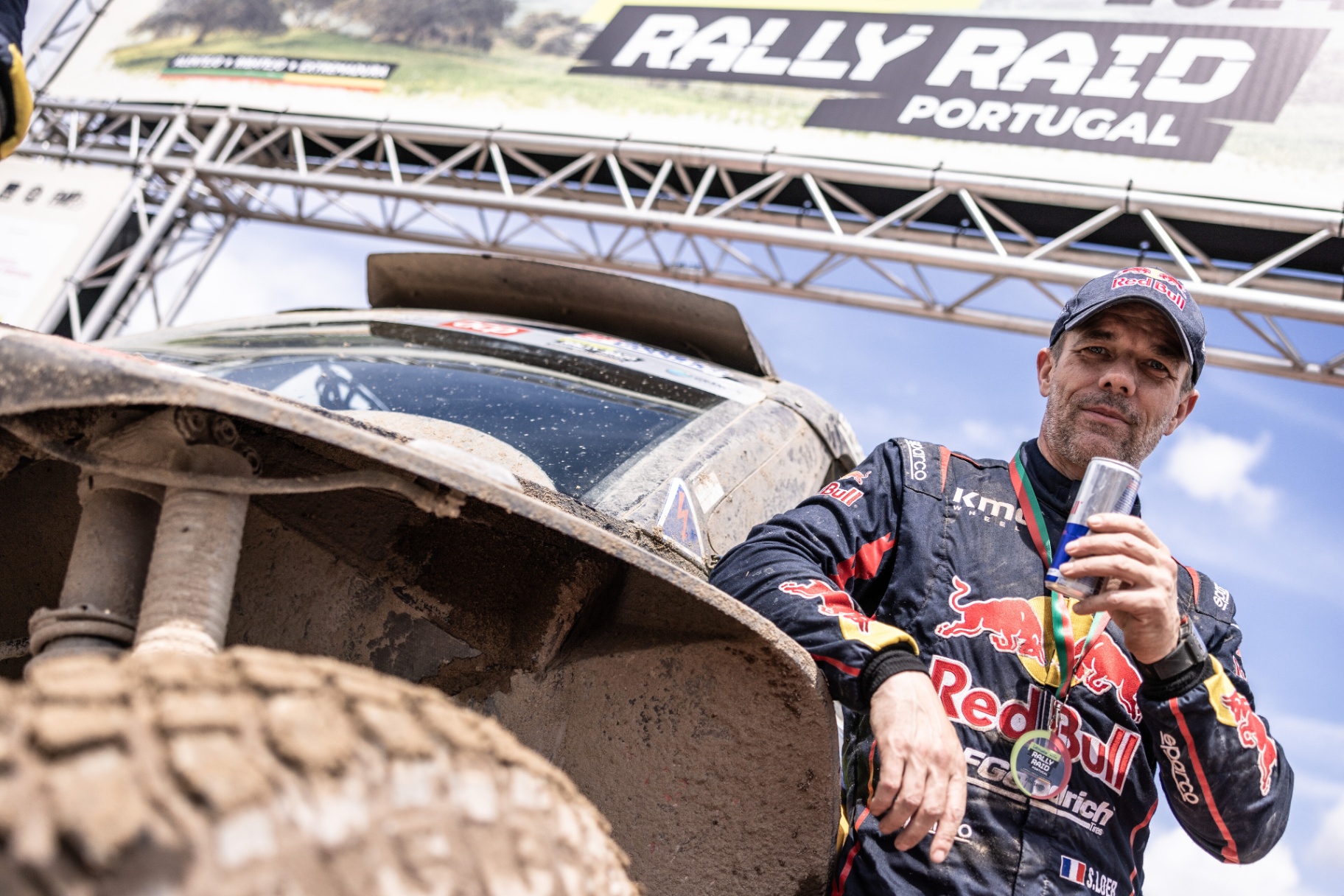 Sébastien Loeb junto à viatura coberta de lama sob o pórtico do Rally Raid Portugal