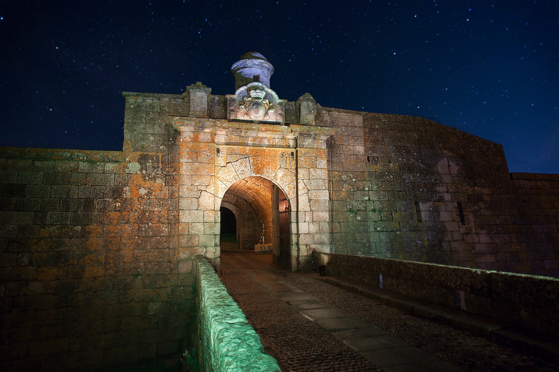 Porta fortificada da praça-forte de Almeida iluminada à noite, com céu estrelado