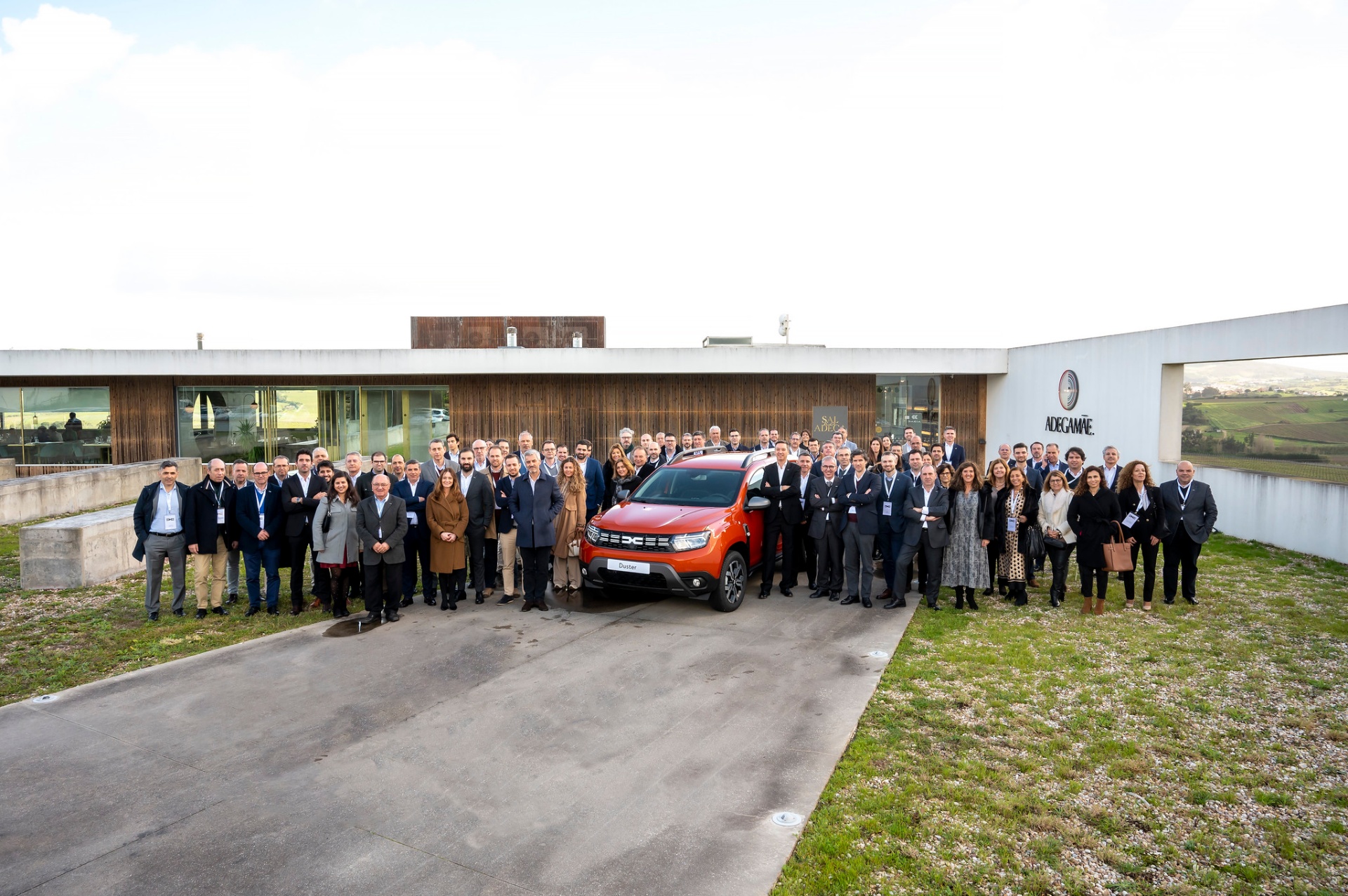 Foto de grupo da rede Dacia em frente à AdegaMãe, com Duster laranja ao centro