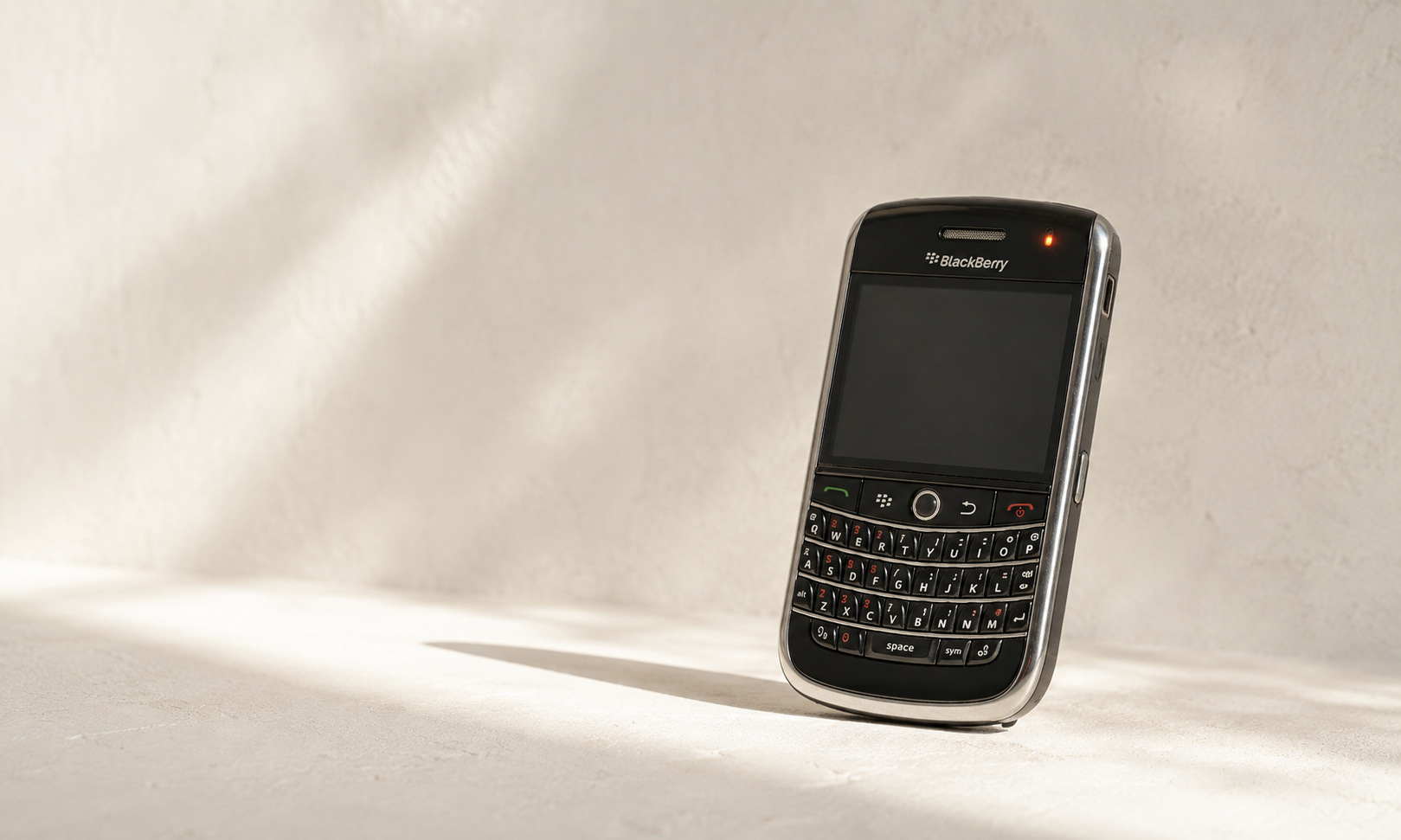 Telemóvel BlackBerry com teclado QWERTY encostado a uma parede clara, iluminado por luz natural