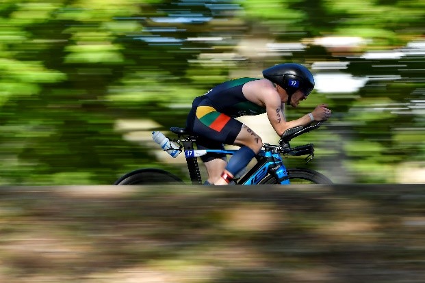 Atleta lituano em bicicleta de triatlo em velocidade num troço arborizado