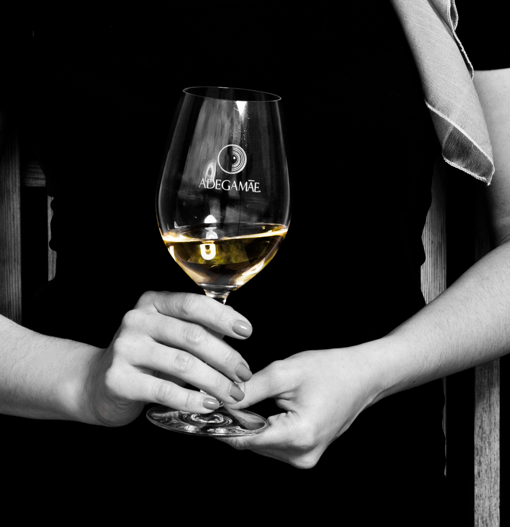 Mãos a segurar copo de prova com vinho branco AdegaMãe