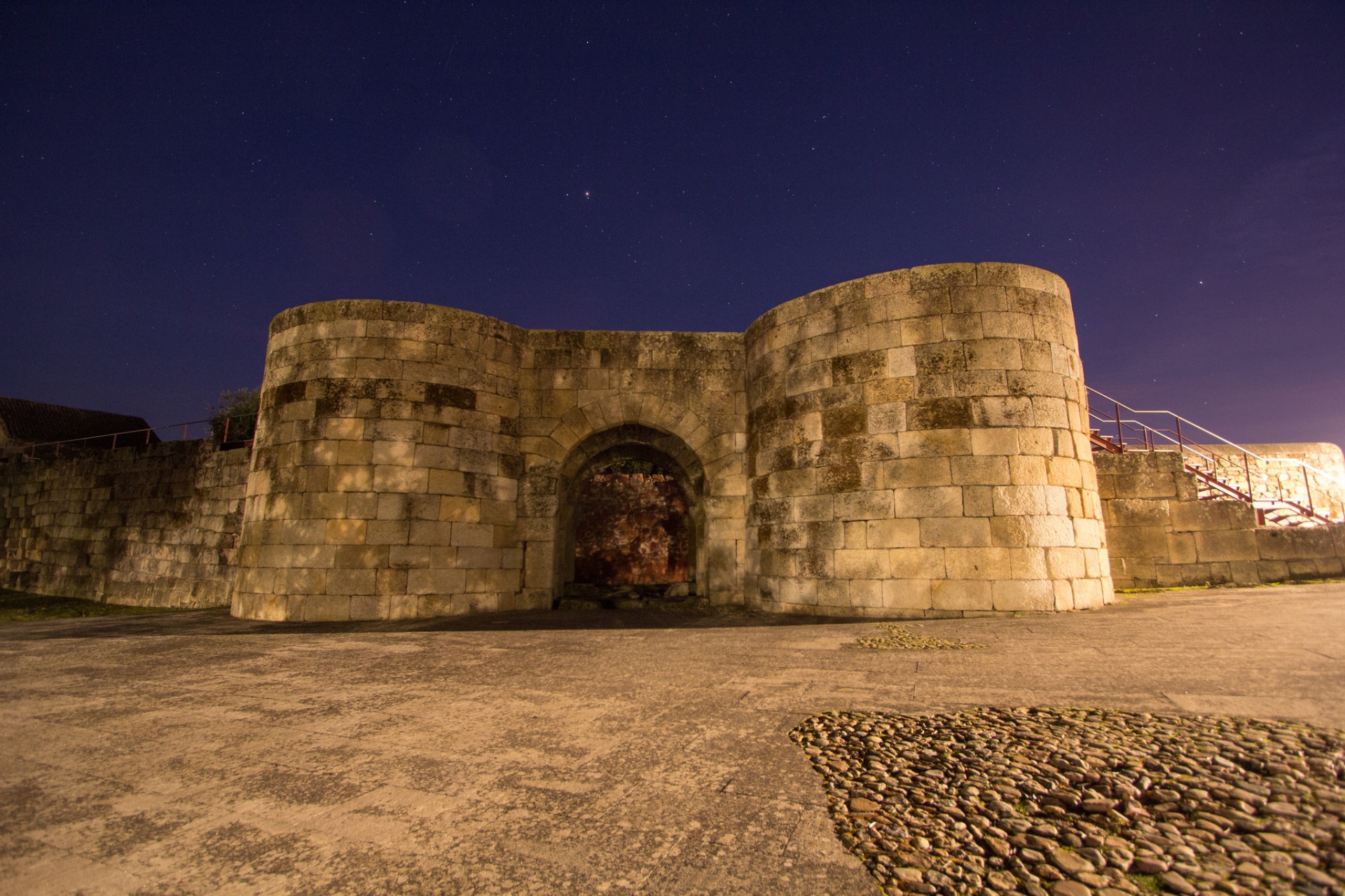 Porta norte da muralha de Idanha-a-Velha iluminada à noite, com céu estrelado