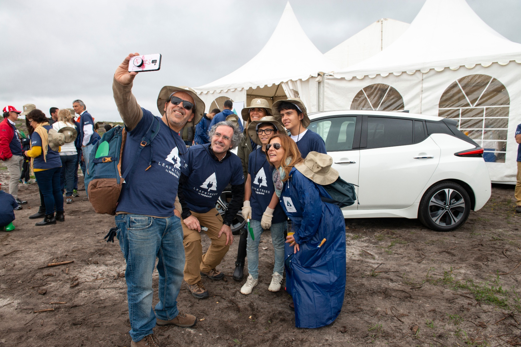 Grupo de voluntários Leaf4Trees a tirar selfie junto a um Nissan Leaf branco e tenda da iniciativa
