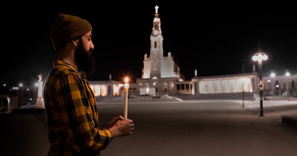 Peregrino com vela acesa frente ao Santuário de Fátima à noite