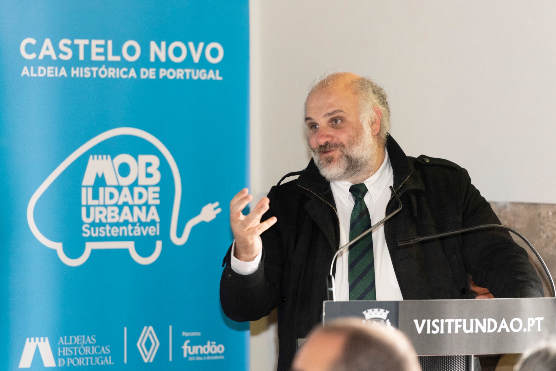 Orador no púlpito da sessão, com roll-up Castelo Novo e logótipo Mobilidade Urbana Sustentável ao lado