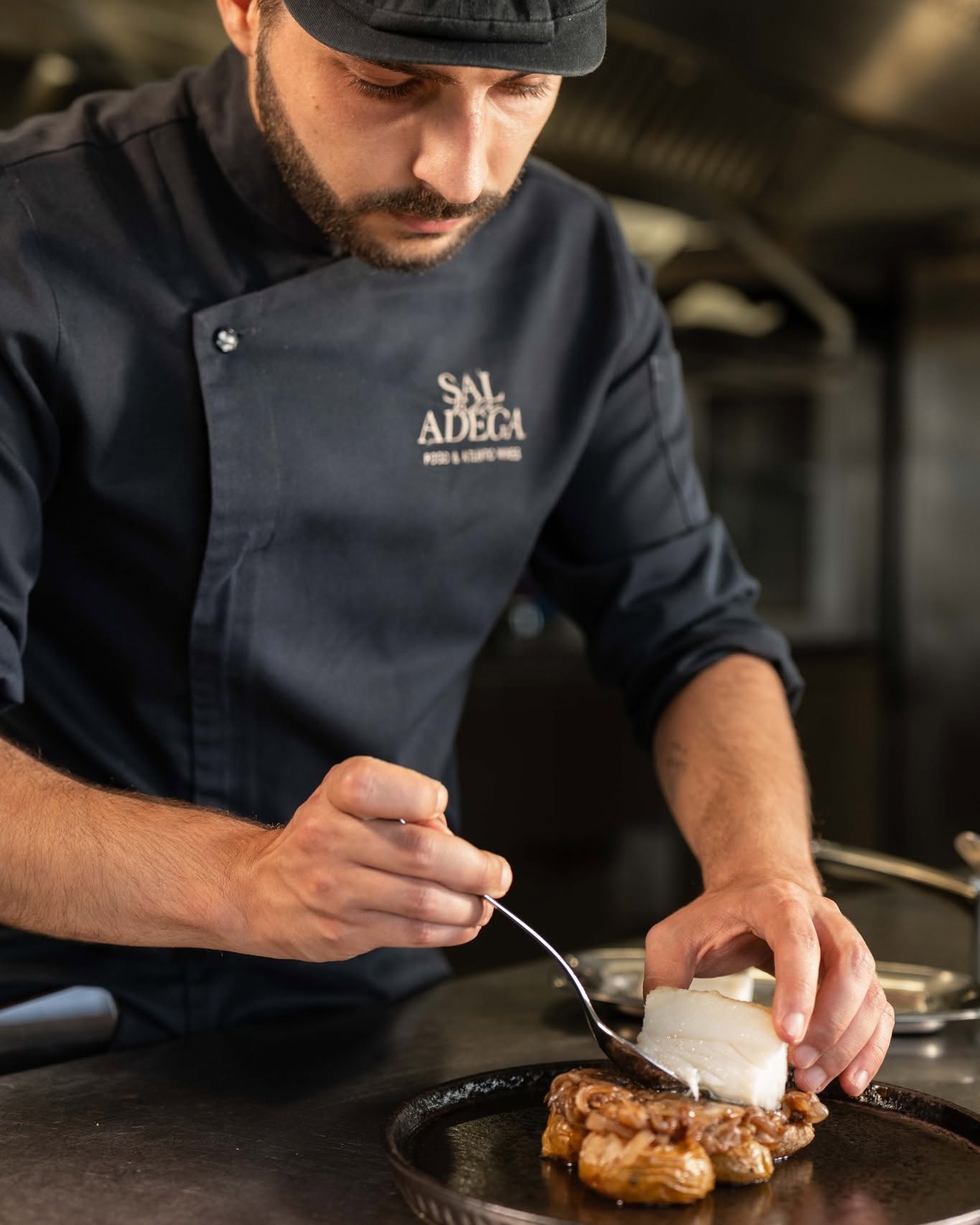 Chef do Sal na Adega a empratar bacalhau sobre cebolada com colher