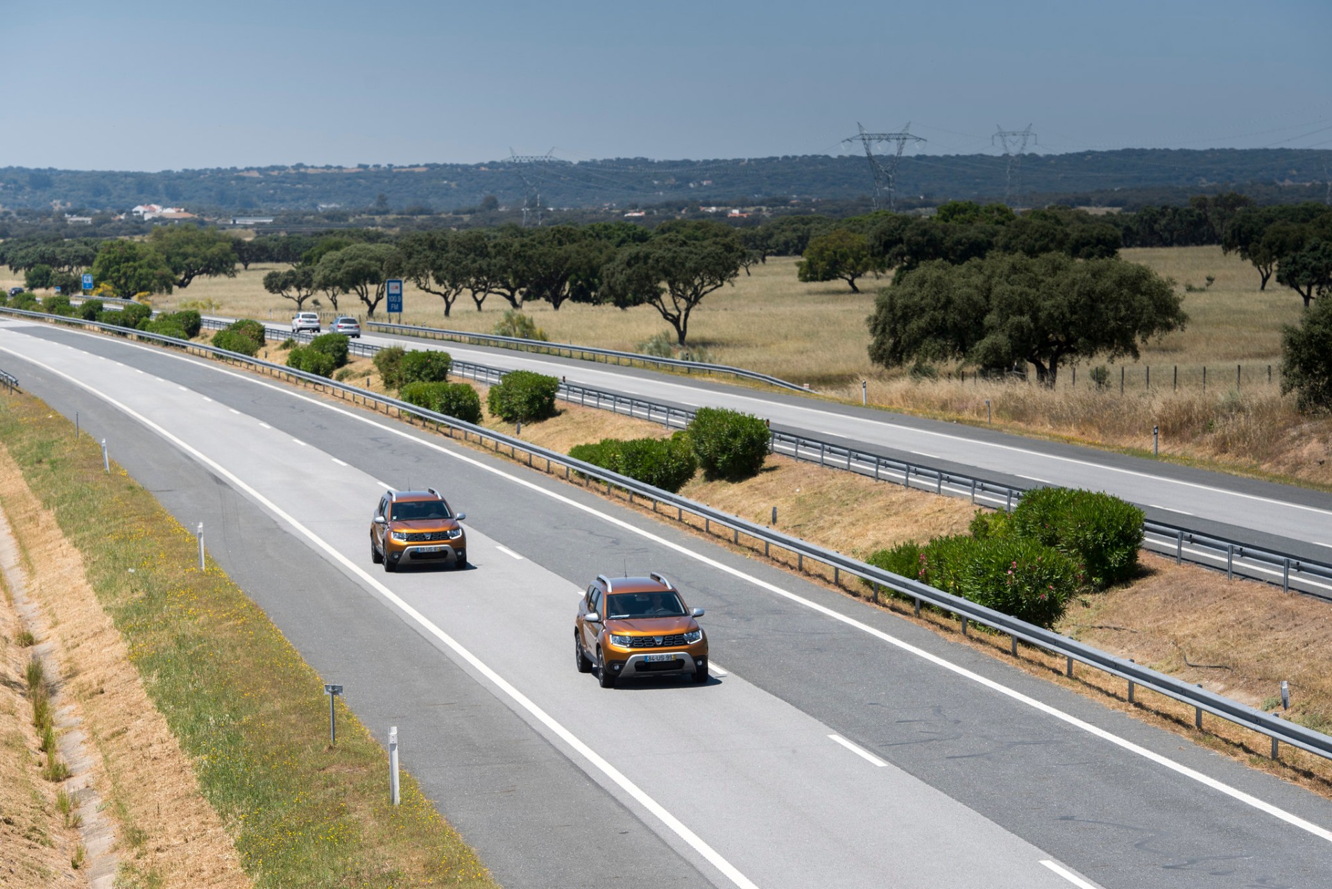 Dois Dacia Duster laranja em autoestrada alentejana com sobreiros ao fundo