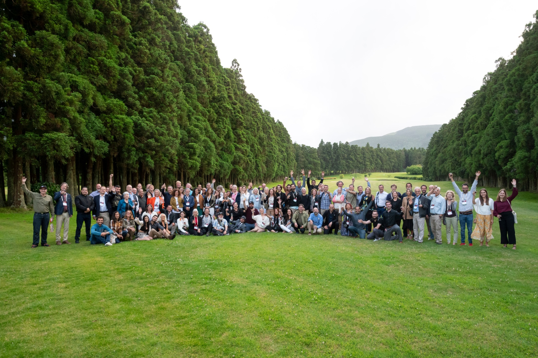 Fotografia de grupo dos participantes da GLEX Summit num campo verde rodeado de criptomérias nos Açores