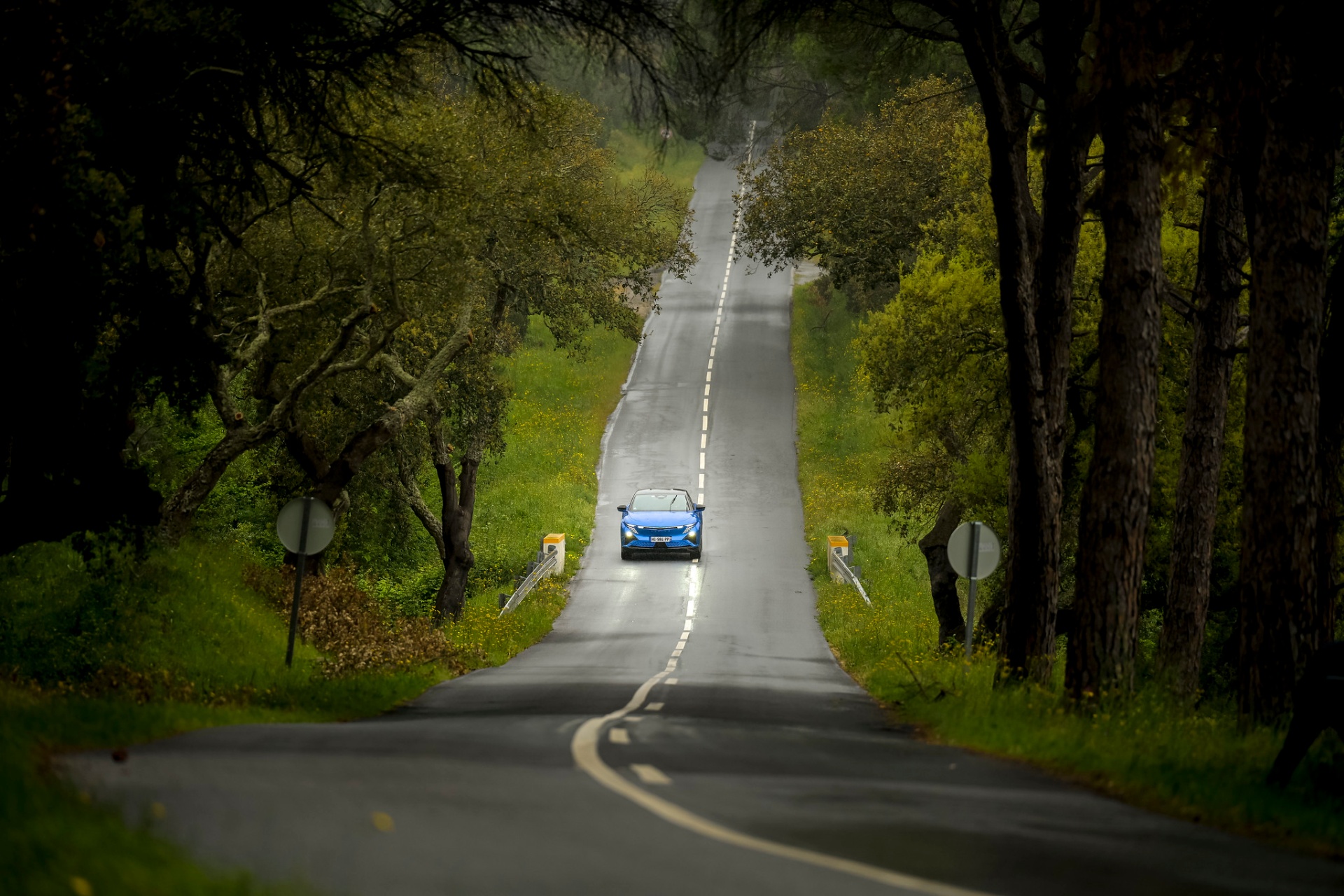 Alpine A390 GT azul ao longe numa estrada rectilínea ladeada por árvores do Alentejo