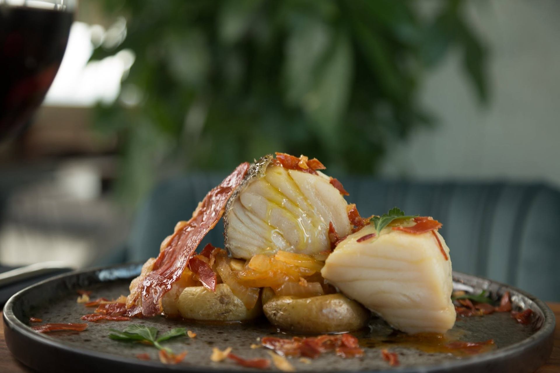 Posta de bacalhau confitado com crocante de presunto, cebolada e batata, servida em prato de pedra