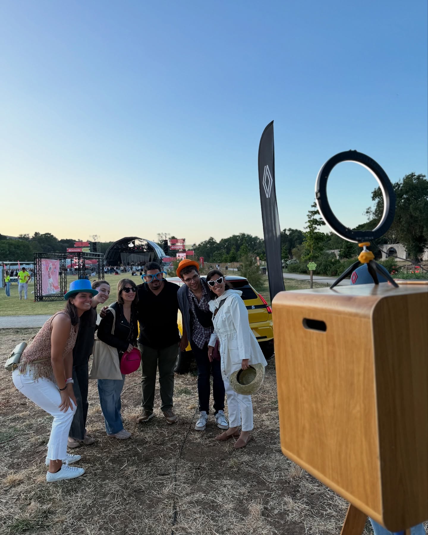 Grupo de visitantes a posar com chapéus e óculos divertidos junto ao photobooth Renault, com o palco do Santander Fest ao fundo