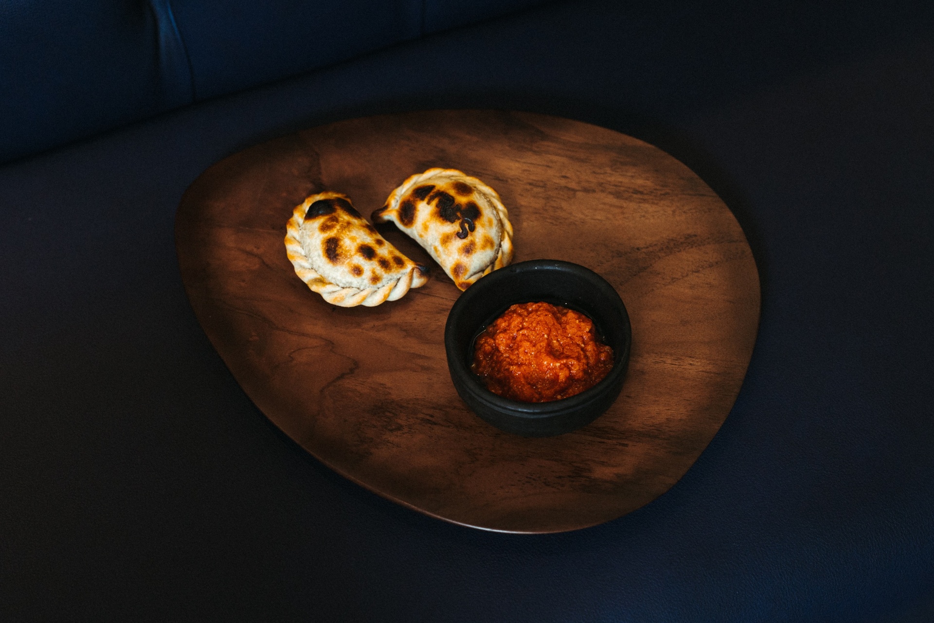 Duas empanadas argentinas tostadas com tigela de molho sobre tábua de madeira